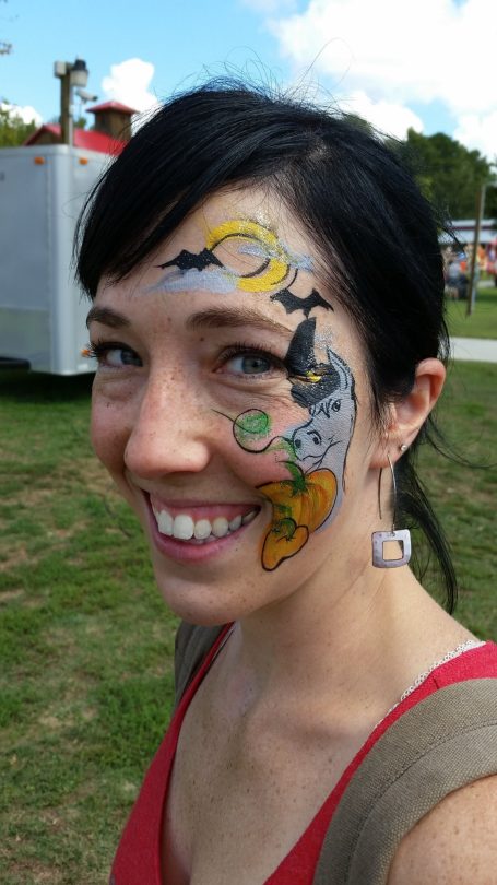 Woman smiling with colorful face paint featuring bats and a pumpkin design.