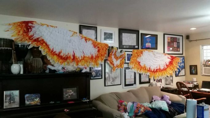 Colorful, fiery wing decorations on a wall with various framed pictures and a couch below.
