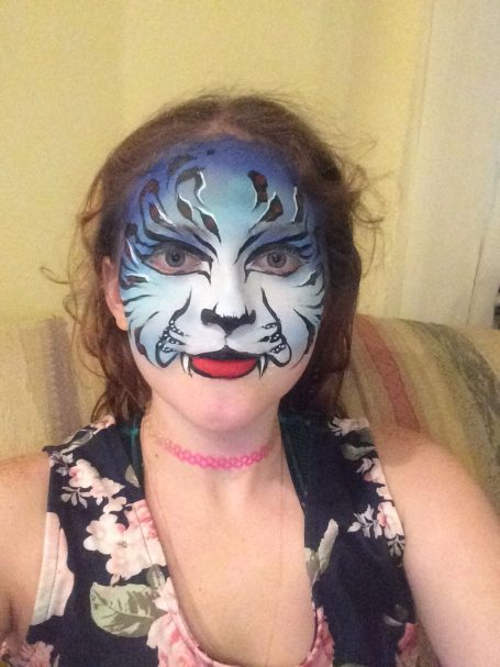 Person with face paint designed to resemble a blue tiger, wearing a floral top.