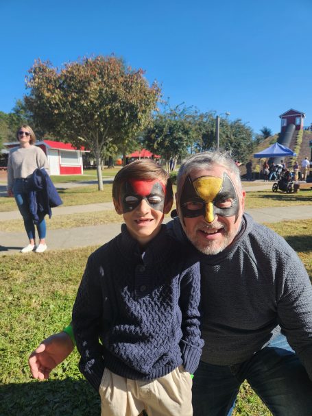 A man and a boy with face paint posing together outdoors on a sunny day.