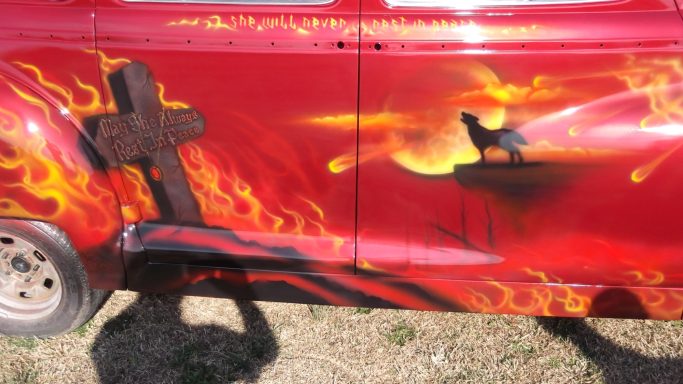 A red car with fiery designs, featuring a cross and a silhouetted lion on a cliff.
