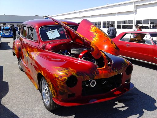 Classic red car with flame graphics and open hood, showcasing its engine.