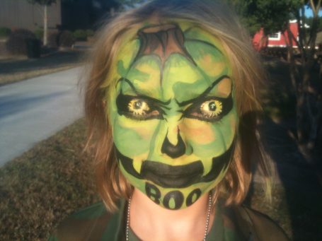 Person with face painted to resemble a green, cartoonish monster with exaggerated features.