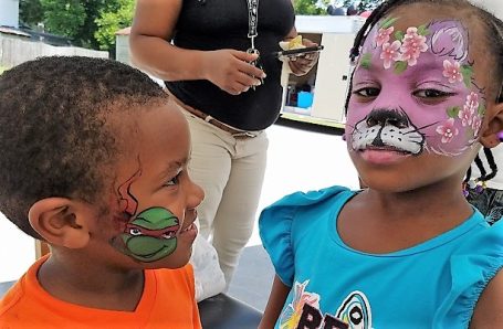Children with face paint, one as a superhero and the other as a cat, smiling.