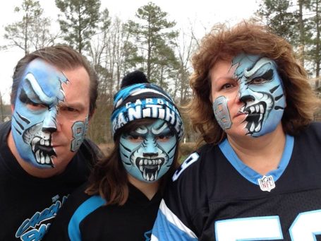 Three people with painted faces in blue and black team colors, wearing team gear.