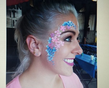 Profile of a woman with colorful flower face paint and bright pink lipstick.