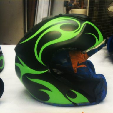 Black helmet with green flame designs and blue accents, partially damaged.