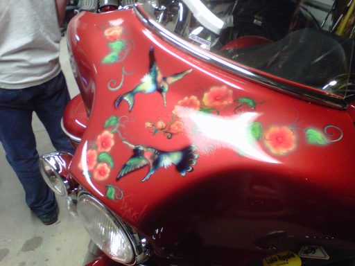 Red motorcycle tank decorated with hummingbirds and roses.