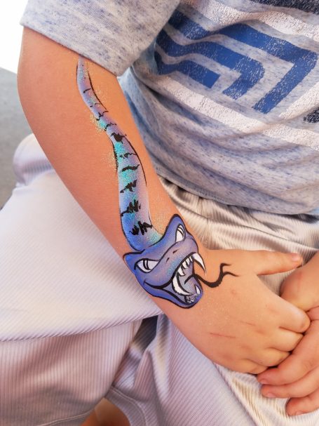 Colorful snake tattoo on a child's arm, featuring a fierce expression and a long, vibrant body.