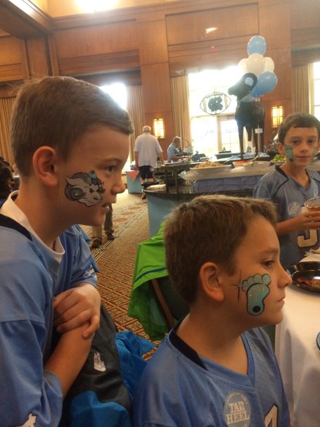 Boys with face paint in blue jerseys at an event, engaging with each other.