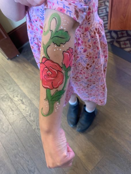 A colorful arm face painting featuring roses and green vines on a person's forearm.
