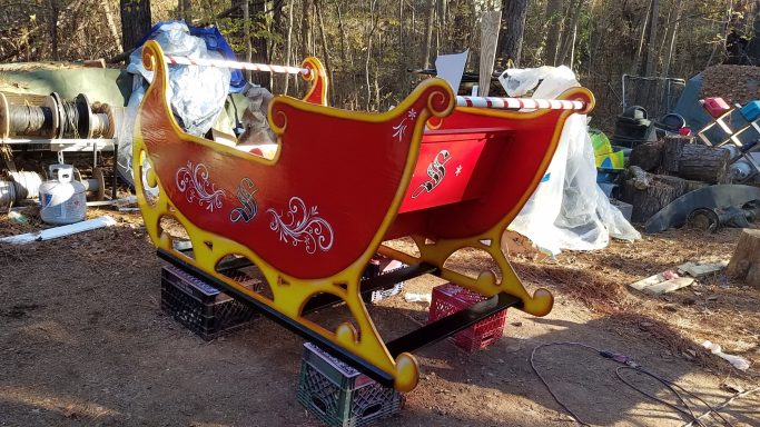 Red and yellow decorative sled in an outdoor setting with clutter in the background.