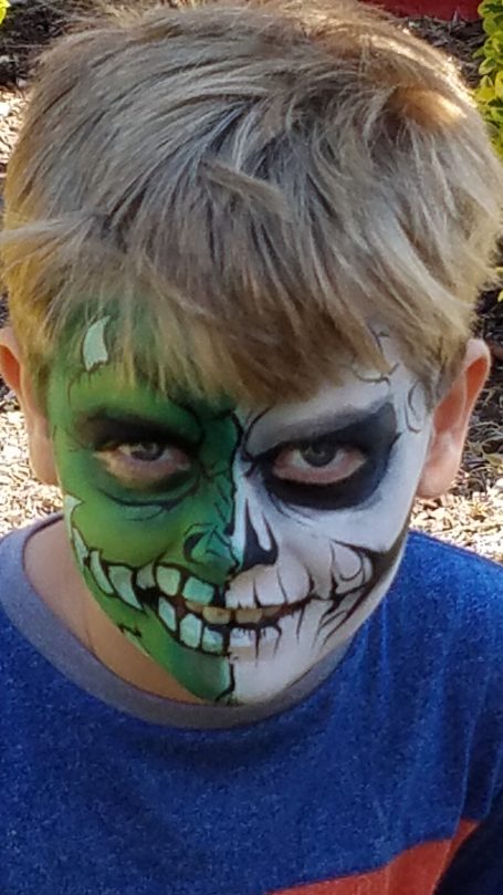 Boy with half face painted green and black, resembling a zombie character.