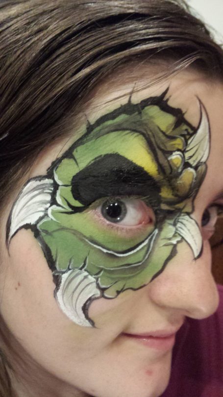 A face painted with a green monster design, highlighting bold features and fangs.