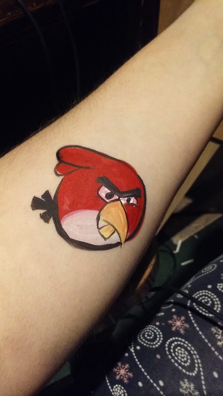 Red cartoon bird face painted on a person's forearm.