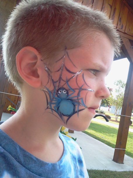 A boy with blue spider web face paint on one side of his face.