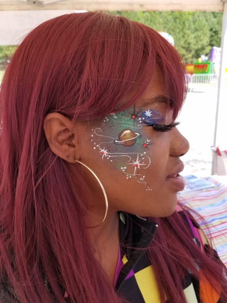 A person with long red hair and artistic face paint showcasing colorful designs.