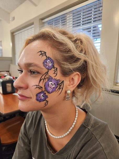 A woman with purple bats face designs on cheek.